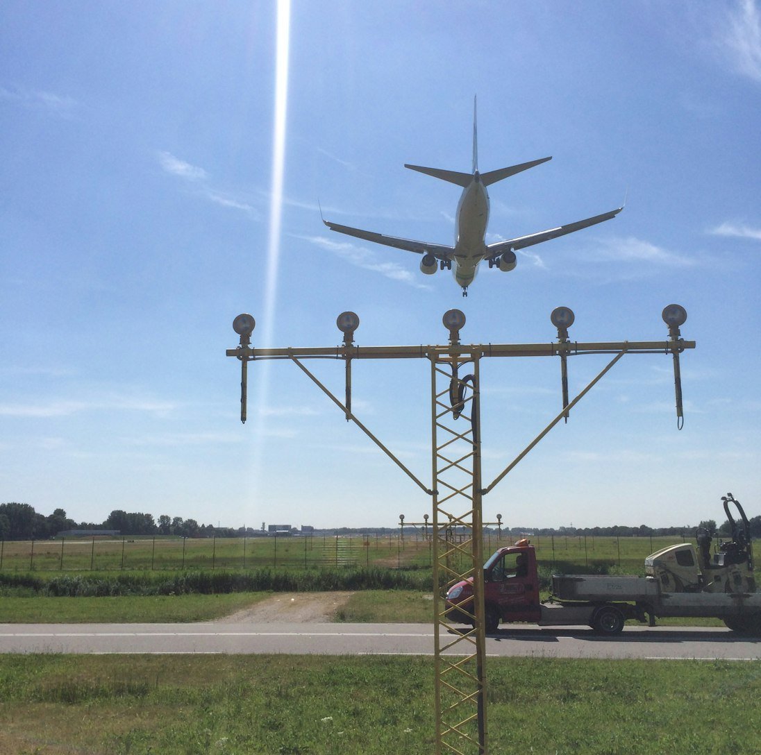 An airplane flying low over an approach light system at an airport under a clear sky.