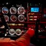 A cockpit panel of dials, gauges and digital displays with a hand gripping the yoke.