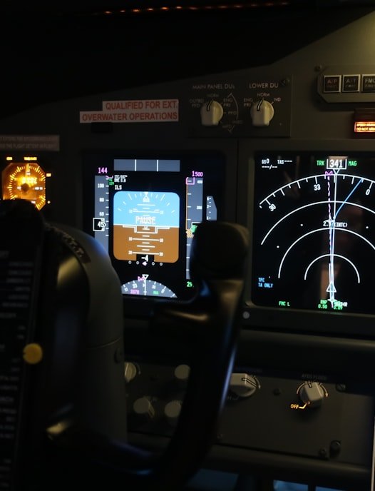 An aircraft cockpit displaying control panels, illuminated instruments, dials and screens showing flight data.