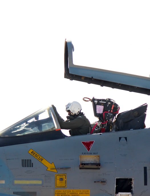 Two pilots wearing helmets seated in the cockpit of a military aircraft with the canopy open.