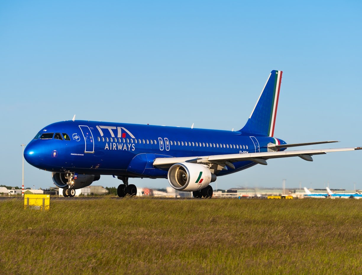 An airplane with a blue fuselage on the runway, positioned on a grassy field with a clear blue sky in the background.
