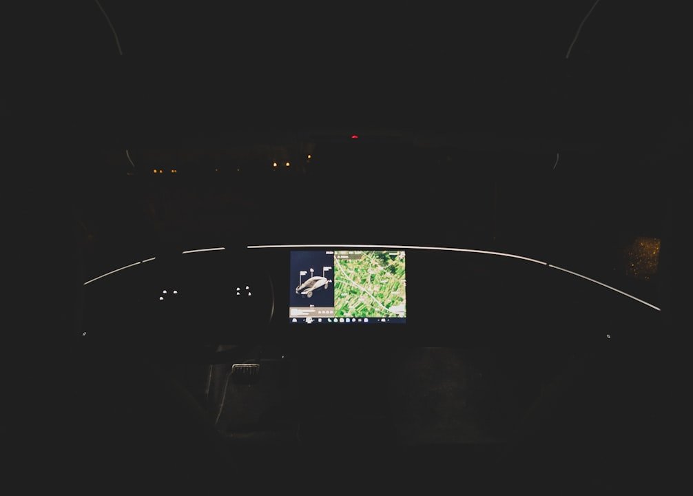 A dimly lit cockpit with a central screen displaying a map and an image of an aircraft, surrounded by unlit controls.